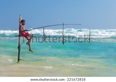 UNAWATUNA, SRI LANKA - MARCH 9, 2014: Young stilt fisherman at Hikkaduwa Beach. Most real stilt fishermen have been long gone. Today it\'s mainly young boys posing as stilt fishermen for tourists.