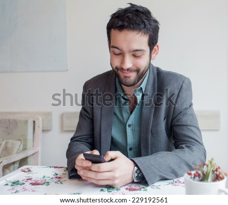Young man wearing jacket sitting in restaurant and typing  on phone.