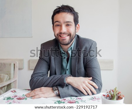 Happy young man wearing jacket sitting in restaurant and smiling.