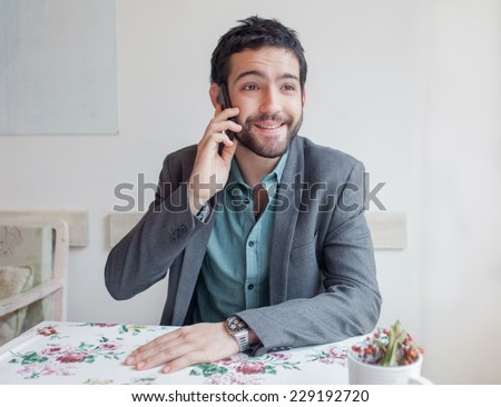 Young man wearing jacket sitting in restaurant and talking on phone.