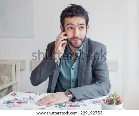 Young man wearing jacket sitting in restaurant and talking on phone.