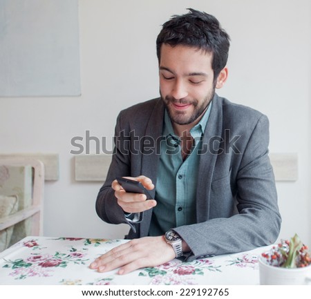 Young man wearing jacket sitting in restaurant and looking on phone.