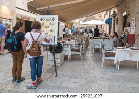DUBROVNIK, CROATIA - MAY 28, 2014: Tourists looking at menu in front of the restaurant terrace. Dubrovnik has many restaurants which offer traditional Dalmatian cuisine and some great wine lists.