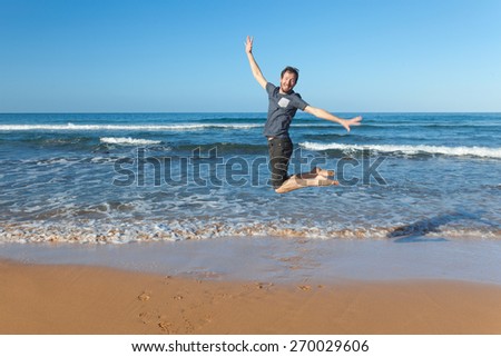 Young happy man jumping at sandy beach.