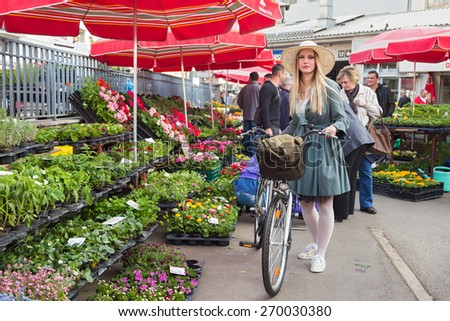 ZAGREB, CROATIA - MARCH 4, 2014: Attractive blonde girl with straw hat and bike on Dolac Market. Dolac has  been the city\'s major trading place since 1926.