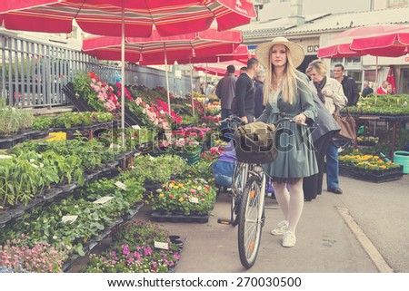 ZAGREB, CROATIA - MARCH 4, 2014: Attractive blonde girl with straw hat and bike on Dolac Market. Dolac has  been the city\'s major trading place since 1926.