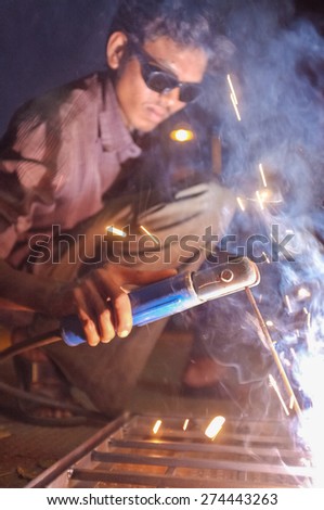 KAMALAPURAM, INDIA - 02 FEBRUARY 2015: Indian worker welding heavy metal parts on street in dusk