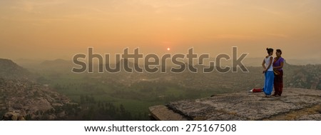 HAMPI, INDIA - 03 FEBRUARY 2015: Two female tourists being photographed by man on hilltop in sunrise