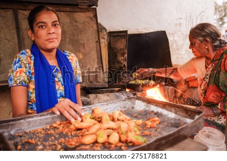 KAMALAPURAM, INDIA - 02 FEBRUARY 2015: Young Indian woman selling fried chilli while her mother makes them in the background