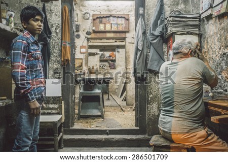 JODHPUR, INDIA - 10 FEBRUARY 2015: Young  boy awaits instructions while carpenter works. Children are used as cheap labourers through out Asia. Post-processed with grain and texture.