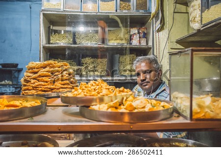 JODHPUR, INDIA - 16 FEBRUARY 2015: Vendor sits in store with various food on metal plates and noodles on shelves. Post-processed with grain and texture.