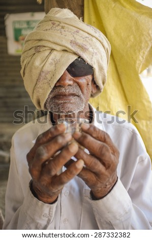 HAMPI, INDIA - 31 JANUARY 2015: Blind elderly indian man with sunglasses and headscarf holding a chai