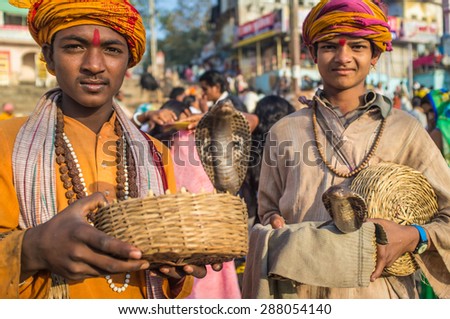 VARANASI, INDIA - 23 FEBRUARY 2015: Two Indian boys dressed up in religious clothes hold cobras in baskets.