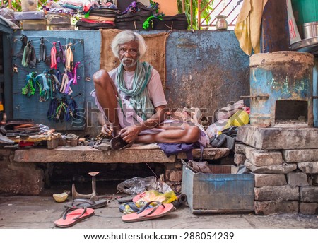 VARANASI, INDIA - 25 FEBRUARY 2015: Indian vendor sits in street shop and repairs slippers.