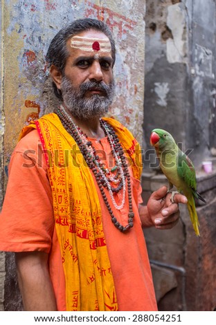 VARANASI, INDIA - 25 FEBRUARY 2015: Indian man pretending to be a sadhu holds parrot in street. Fake holy men are common on India\'s streets.