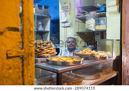 JODHPUR, INDIA - 16 FEBRUARY 2015: Vendor sits in store with food on metal plates.