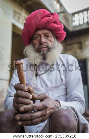 GODWAR REGION, INDIA - 12 FEBRUARY 2015: Elderly Rabari tribesman with traditional turban, clothes and long beard holds chillum. Hands in focus. Rabari or Rewari are an Indian community in Gujarat.