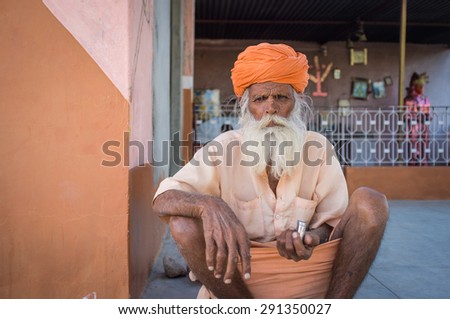 GODWAR, INDIA - 12 FEBRUARY 2015: Elderly Indian tribesman with turban in lungi sits on ground in front of temple.