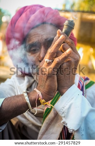 GODWAR REGION, INDIA - 14 FEBRUARY 2015: Elderly Rabari tribesman with red turban and blanket smokes chillum. Rabari or Rewari are an Indian community in the state of Gujarat.