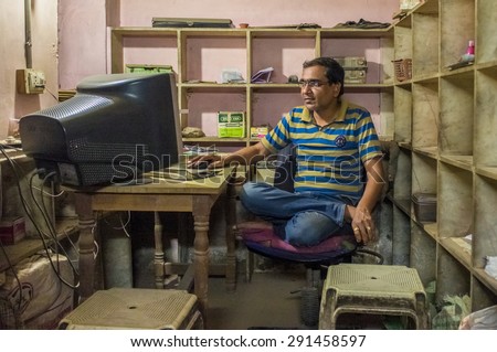 JODHPUR, INDIA - 16 FEBRUARY 2015: Indian man sits in office cross-legged on chair in front of computer screen.