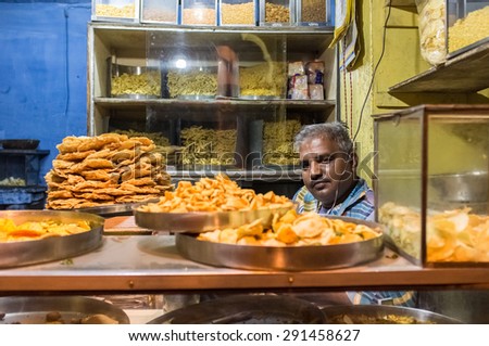 JODHPUR, INDIA - 16 FEBRUARY 2015: Vendor sits in store with various food on metal plates and noodles on shelves.
