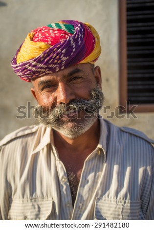 GODWAR REGION, INDIA - 14 FEBRUARY 2015: Adult Indian man with colorful turban and curled mustache sits in street.
