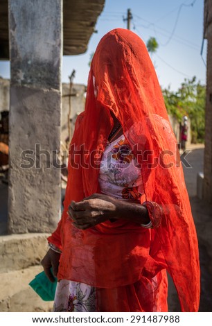 GODWAR REGION, INDIA - 13 FEBRUARY 2015: Indian woman in orange sari with covered head stands in village street.