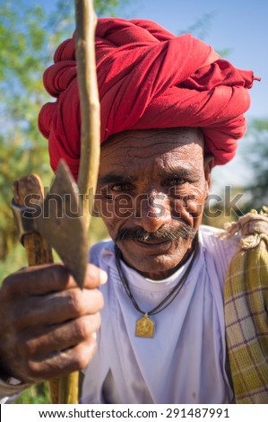 GODWAR REGION, INDIA - 14 FEBRUARY 2015: Elderly Rabari tribesman with red turban sits and holds axe and stick. Rabari or Rewari are an Indian community in the state of Gujarat.