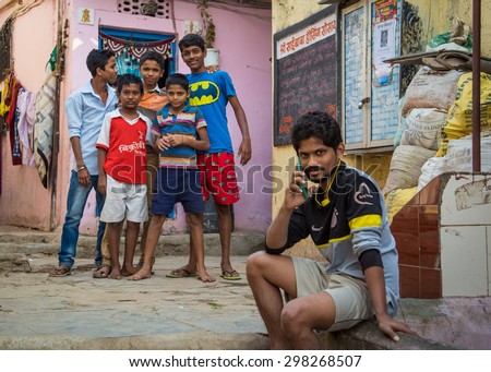 MUMBAI, INDIA - 16 JANUARY 2015: Five boys stand together in slum street while older boy talks on cellphone.