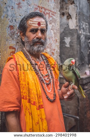 VARANASI, INDIA - 25 FEBRUARY 2015: Indian man pretending to be a sadhu holds parrot that shows wings. Post-processed with grain, texture and colour effect.