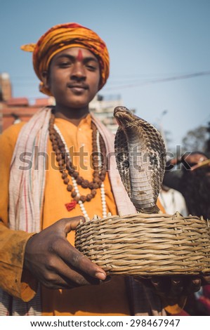 VARANASI, INDIA - 23 FEBRUARY 2015: Indian boy dressed up in religious clothes holds cobra in basket. Post-processed with grain, texture and colour effect.