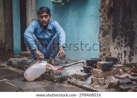 MUMBAI, INDIA - 12 JANUARY 2015: Young Indian man fills water tank in street. Dharavi slum mostly has drinkable water. Post-processed with grain, texture and colour effect.