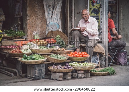 MUMBAI, INDIA - 17 JANUARY 2015: Elderly Indian man writes in book and waits for customer next to grocery shop in market street. Post-processed with grain, texture and colour effect.