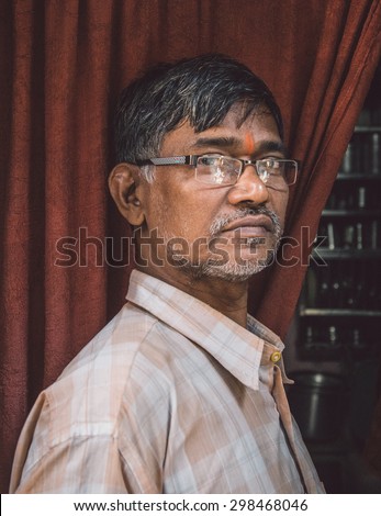 MUMBAI, INDIA - 12 JANUARY 2015: Elderly Indian man with glasses and bindi stands in doorway of home. Post-processed with grain, texture and colour effect.