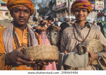 VARANASI, INDIA - 23 FEBRUARY 2015: Two Indian boys dressed up in religious clothes hold cobras in baskets. Post-processed with grain, texture and colour effect.