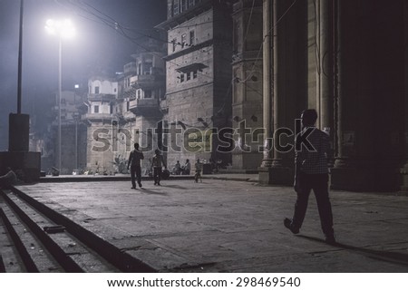 VARANASI, INDIA - 20 FEBRUARY 2015: Man walks towards people on Varanasi ghats at night. Post-processed with grain, texture and colour effect.