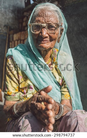 GODWAR REGION, INDIA - 13 FEBRUARY 2015: Elderly Indian woman in sari with covered head and repaired glasses sits in doorway of home. Post-processed with grain, texture and colour effect.