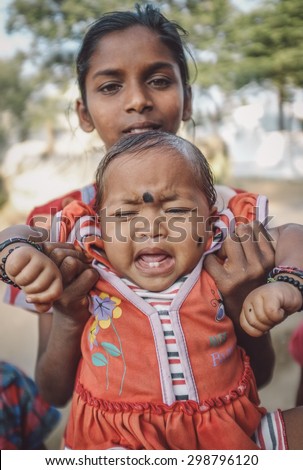 HAMPI, INDIA - 31 JANUARY 2015: Indian baby with bindi cries while being held by family member. Post-processed with grain, texture and colour effect.