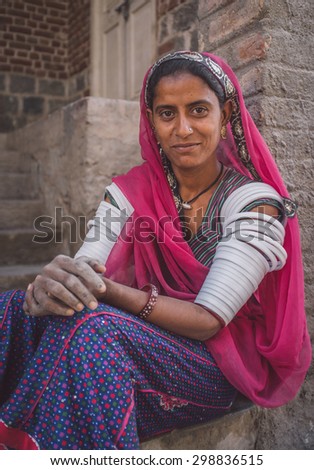 GODWAR REGION, INDIA - 15 FEBRUARY 2015: Indian tribeswoman sitting in front of home in saree decorated with upper-arm bracelets. Post-processed with grain, texture and colour effect.