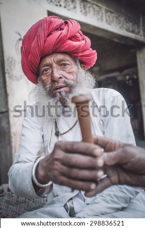 GODWAR REGION, INDIA - 12 FEBRUARY 2015: Elderly Rabari tribesman with traditional turban, clothes and long beard hands out chillum. Post-processed with grain, texture and colour effect.