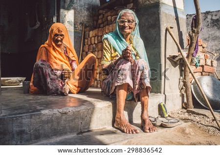 GODWAR REGION, INDIA - 13 FEBRUARY 2015: Two elderly Indian woman in sari\'s with covered heads sit in doorway of home. Post-processed with grain, texture and colour effect.