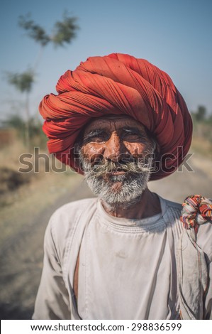 GODWAR REGION, INDIA - 14 FEBRUARY 2015: Elderly Rabari tribesman with big red turban stands on road. Post-processed with grain, texture and colour effect.