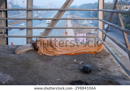 MUMBAI, INDIA - 05 FEBRUARY 2015: Person sleeps on overpass on dirty ground with whole body covered under blanket. Common scene on India\'s streets.