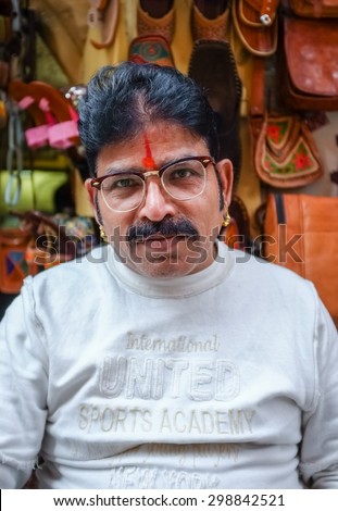 JODHPUR, INDIA - 07 FEBRUARY 2015: Store owner with mustache wearing glasses, gold earings and bindi sitting infront of shop. Rajasthan is known for leather designs than are sold around the country.