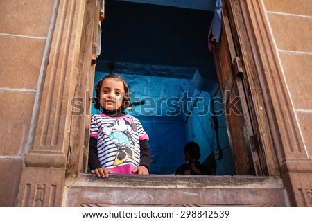 JODHPUR, INDIA - 07 FEBRUARY 2015: Little girl in Minnie Mouse shirt looking through window in blue-painted room. Common scene of blue-painted walls inside and outside of homes in old part of Jodhpur.