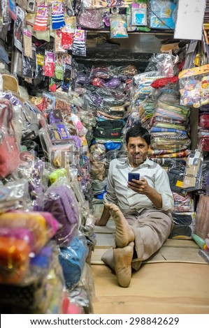 JODHPUR, INDIA - 07 FEBRUARY 2015: Store owner sitting on floor of clothing shop with mobile phone while waiting for customers. Little local textile shop overflown with different merchandise.