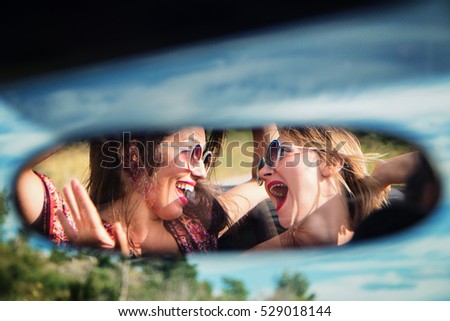 Two happy girls in a car rear-view mirror.