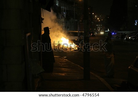 silhouette of hasidic jew standing in front of blazing riot fires, jerusalem, israel
