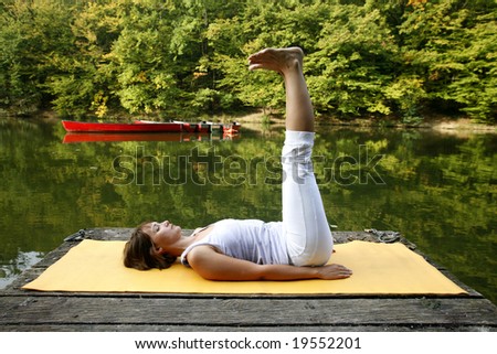 Woman doing yoga on lake in park in autumn