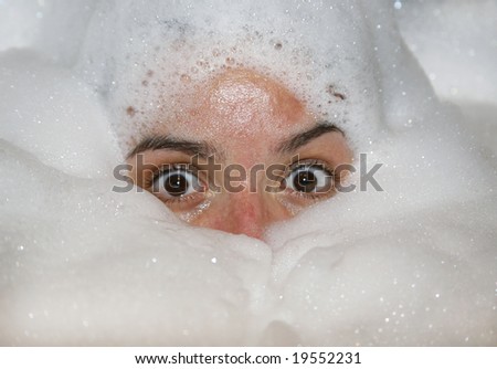 Woman with wide open eyes in foamy bath tub
